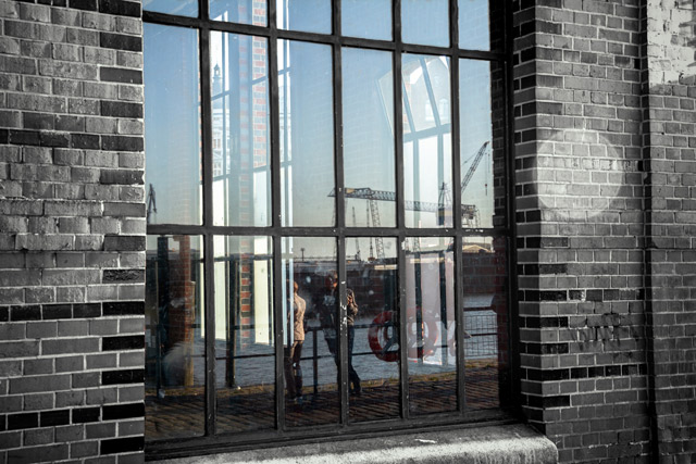 eine-mauer-und-ein-fabrikfenster-in-der-sich-zwei-menschen-spiegeln